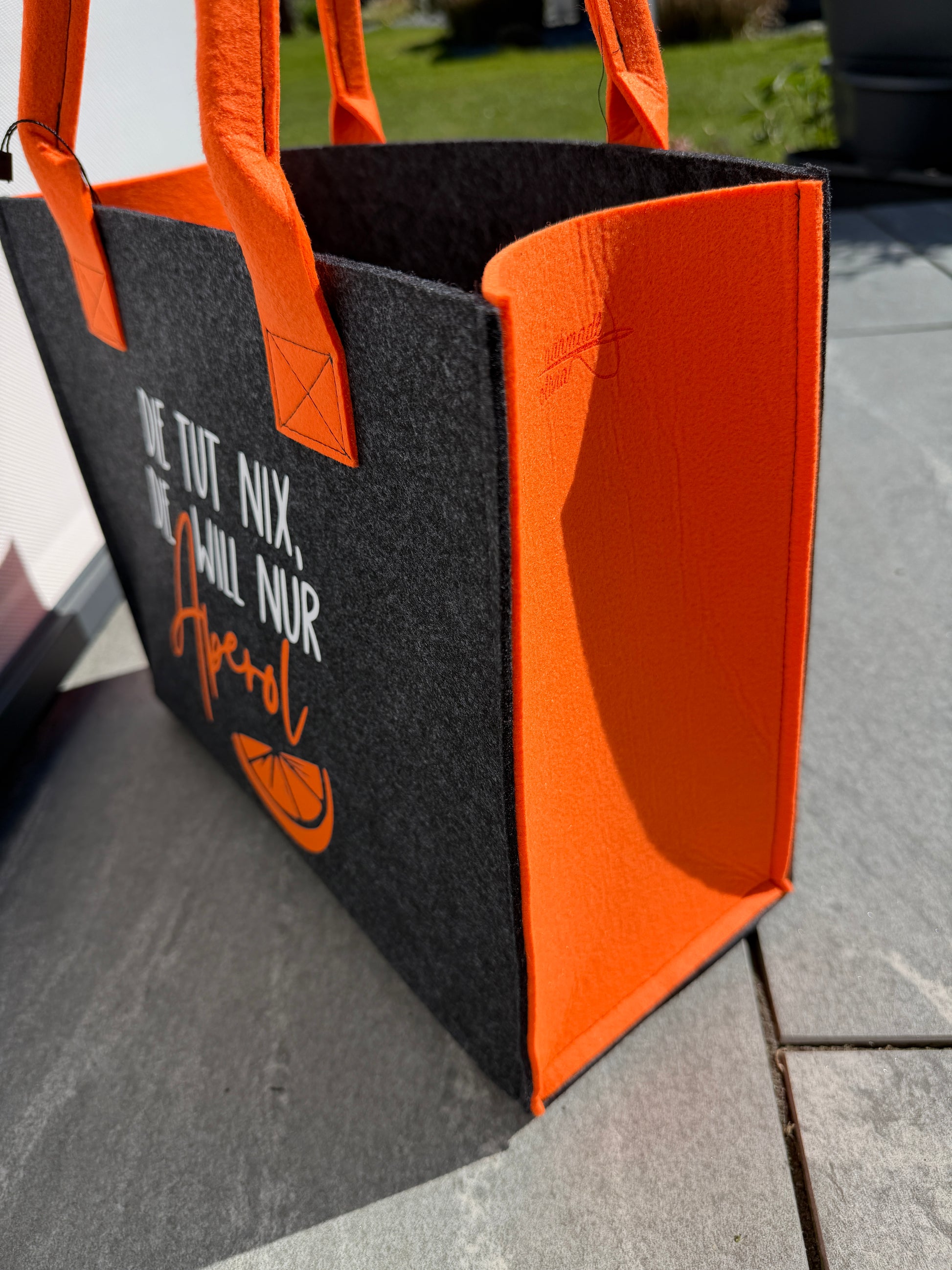 Handgefertigte anthrazitfarbene Filztasche mit orangenen Tragegriffen und dem Spruch „Die tut nix, die will nur Aperol.“ – die perfekte Tasche für Camping und Sommer.